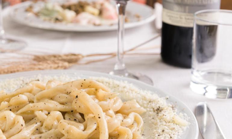 Pasta cacio e pepe con vino rosso su tavola apparecchiata.