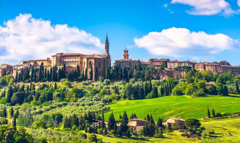 Panorama collinare con edifici storici e cipressi sotto un cielo blu.