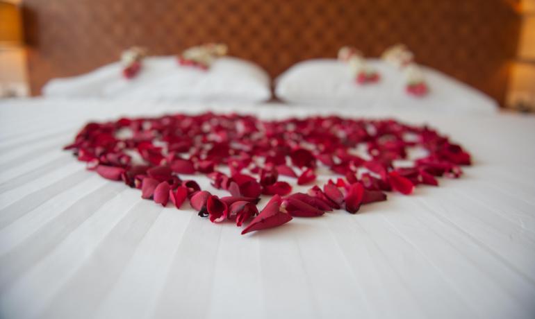 Rose petals arranged in a heart shape on a white bed.