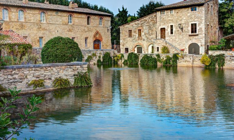 Antico borgo toscano con terme e riflessi d'acqua.