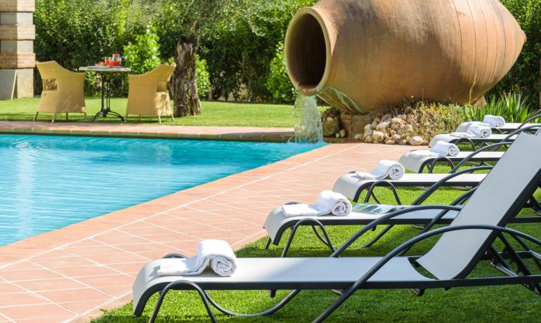 Piscina con lettini, anfora e tavolo con sedie nel giardino.