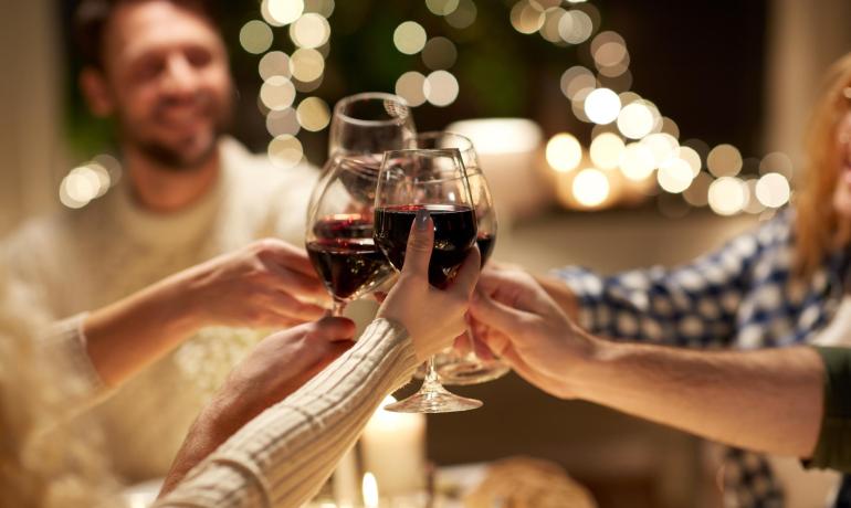 Amici brindano con bicchieri di vino rosso, luci soffuse sullo sfondo.