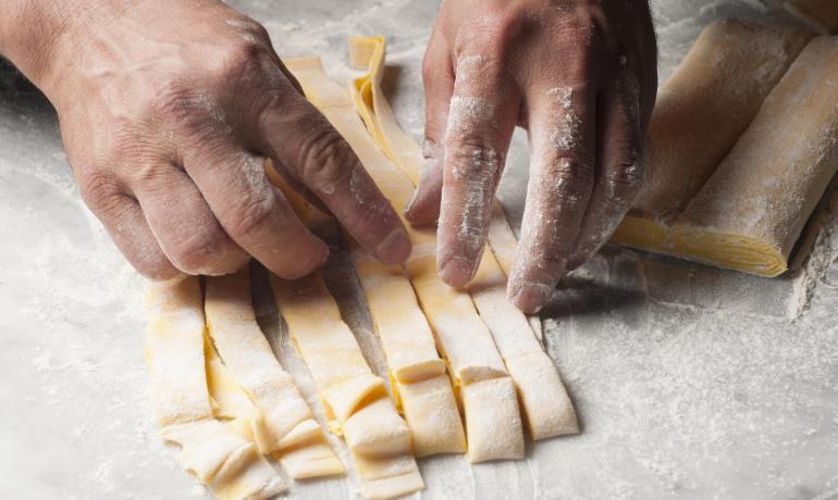 Hands cutting fresh pasta on a floured surface.